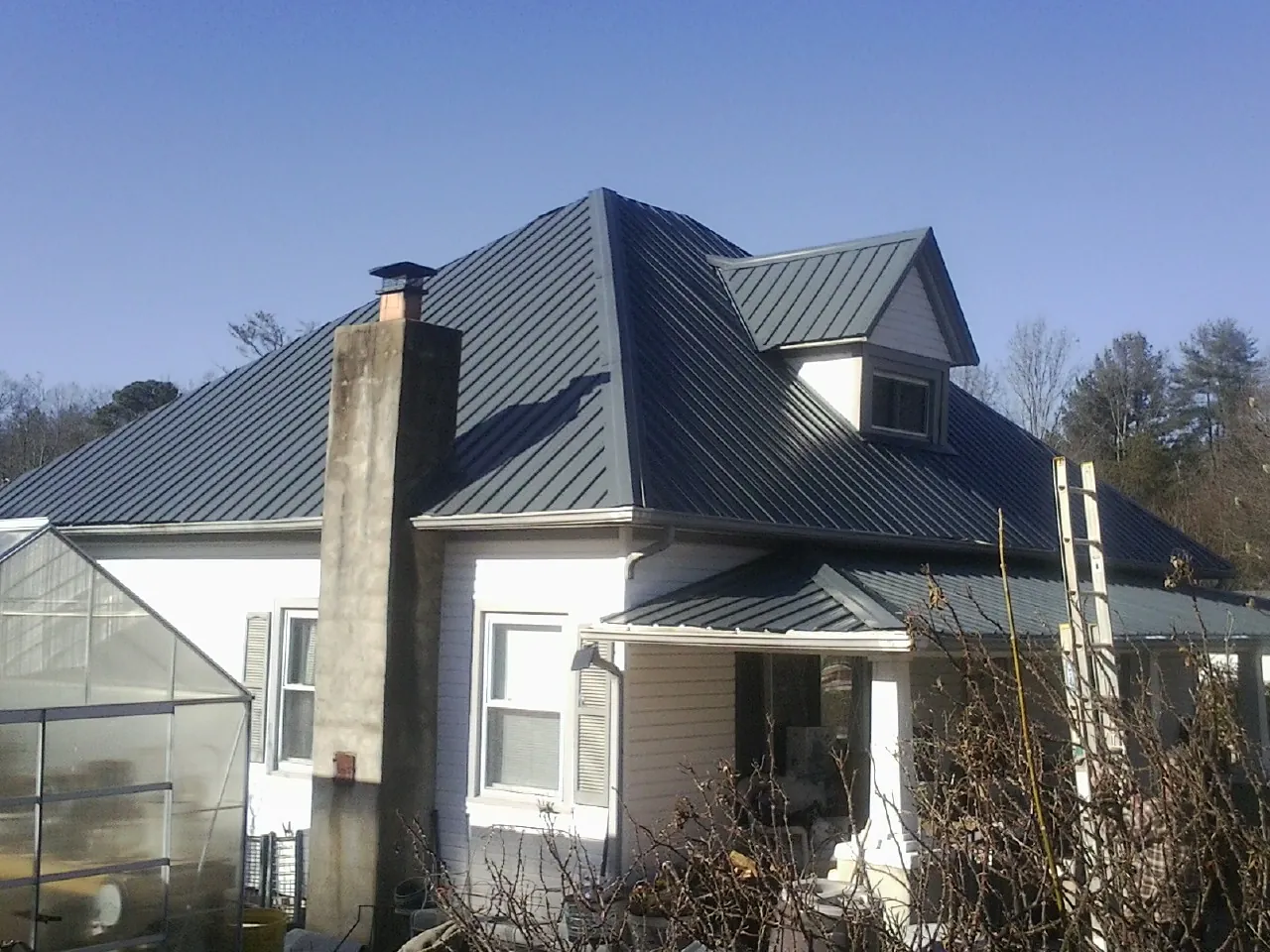 Dark blue standing seam metal roof on a white farmhouse with dormer — Slate & Tile Roof Repair by Roofing Brothers in Trout Lake