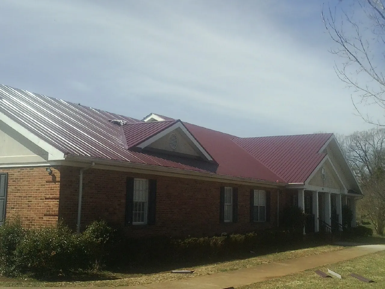 Red metal roof with gabled entries on a long brick building, from a Hail Damage Roof Repair job in Trout Lake