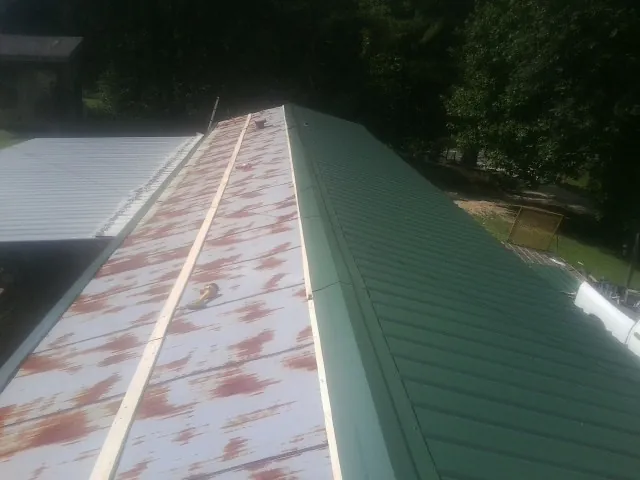 Old rusted panels beside newly installed green metal roofing — Wind Damage Roof Repair by Roofing Brothers in Trout Lake