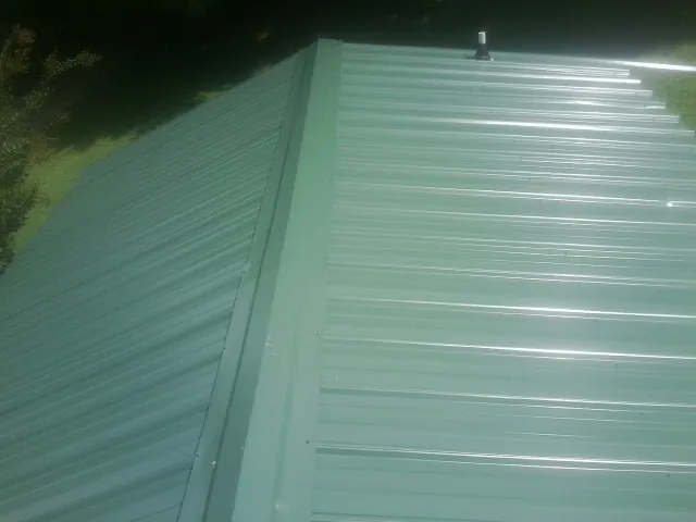 New green metal panels meeting at the ridge of a roof — Flat Roof Repair work by our crew in Trout Lake