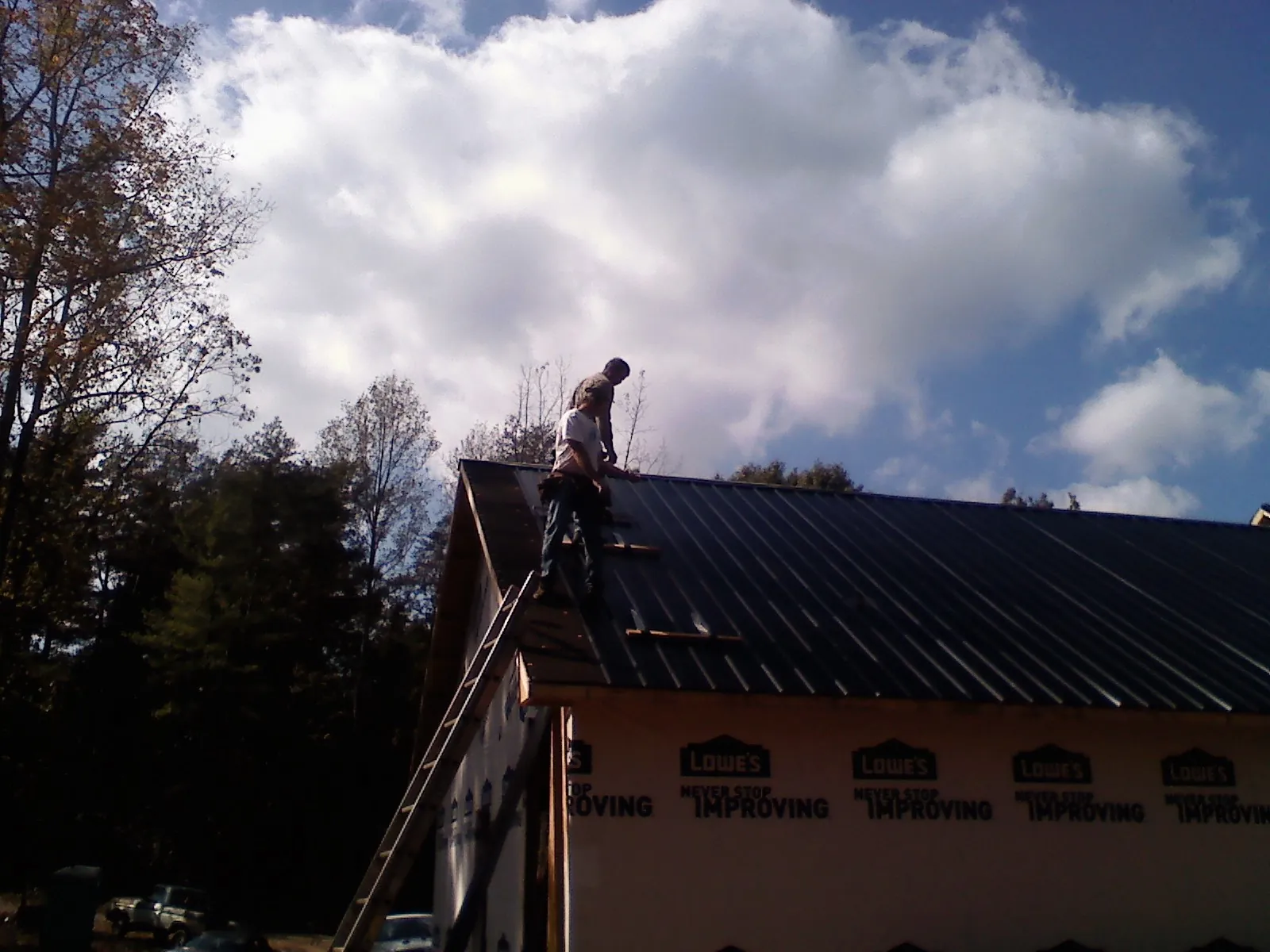 Roofer fastening dark metal panels high against a cloudy sky, from a Roof Inspection job in Trout Lake