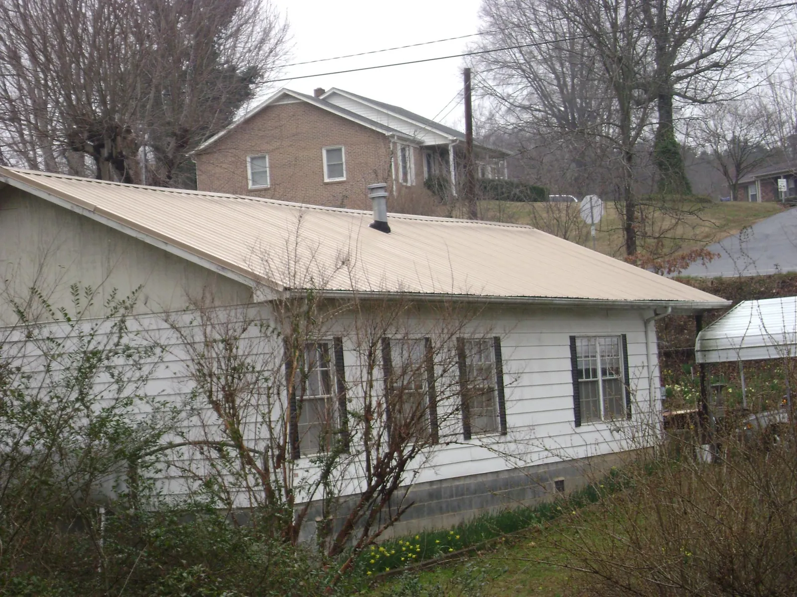 Tan metal roof on a white sided house set into a hillside — Commercial Roofing by Roofing Brothers in Trout Lake