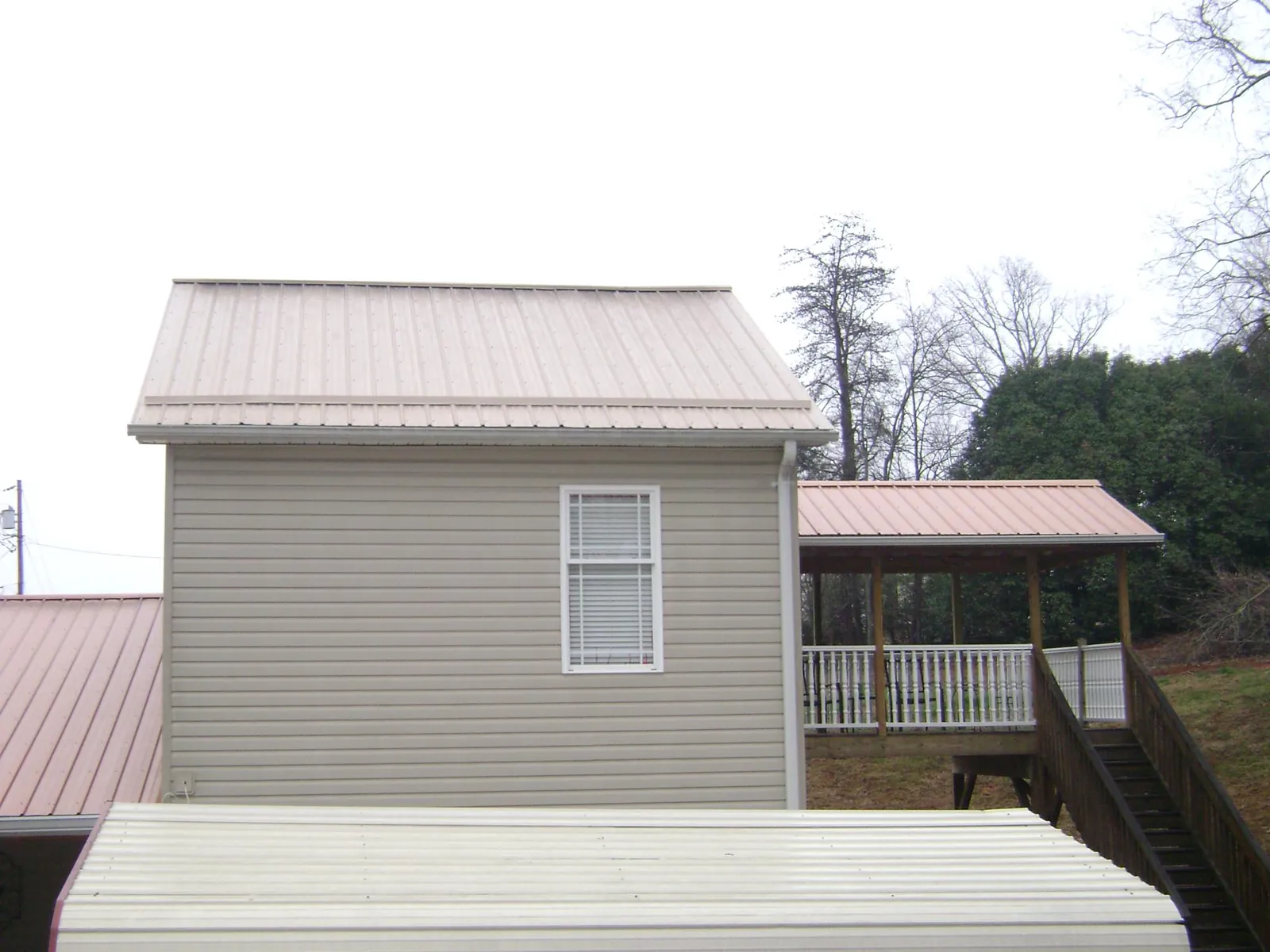 Tan metal roofs on a two story addition and attached porch, from a Roof Replacement job in Trout Lake